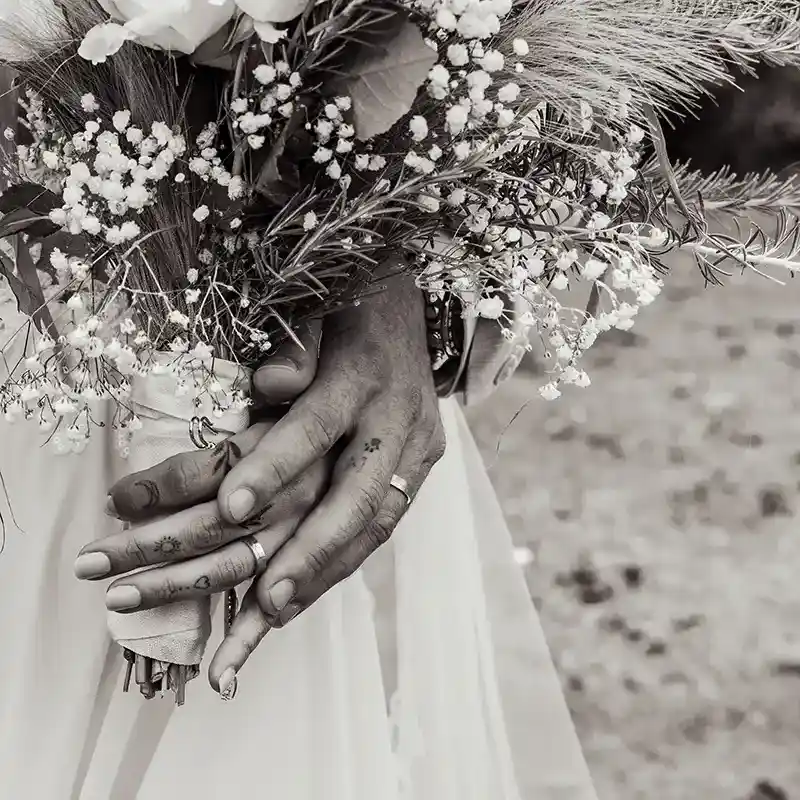 die Hände von einem Brautpaar mit Brautstrauß