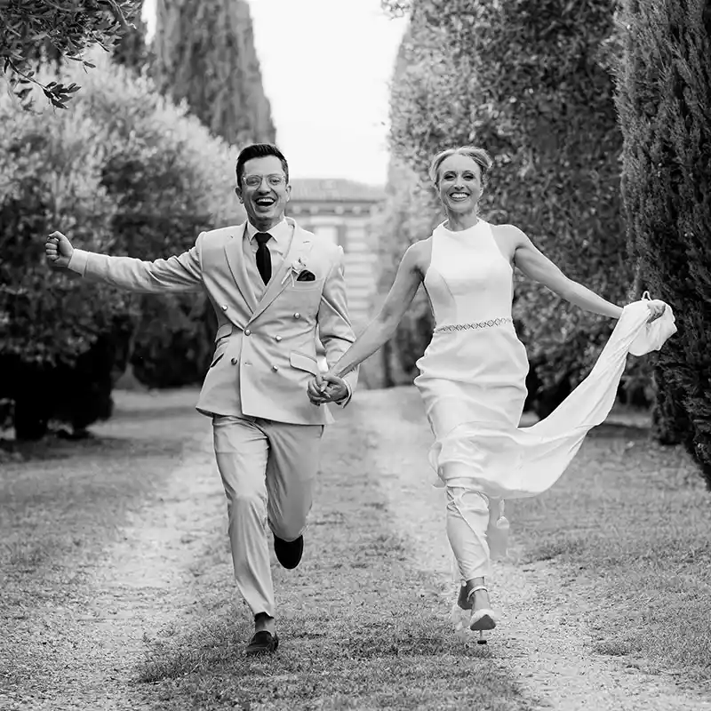 jubelndes Brautpaar rennt eine Allee entlang in Italien